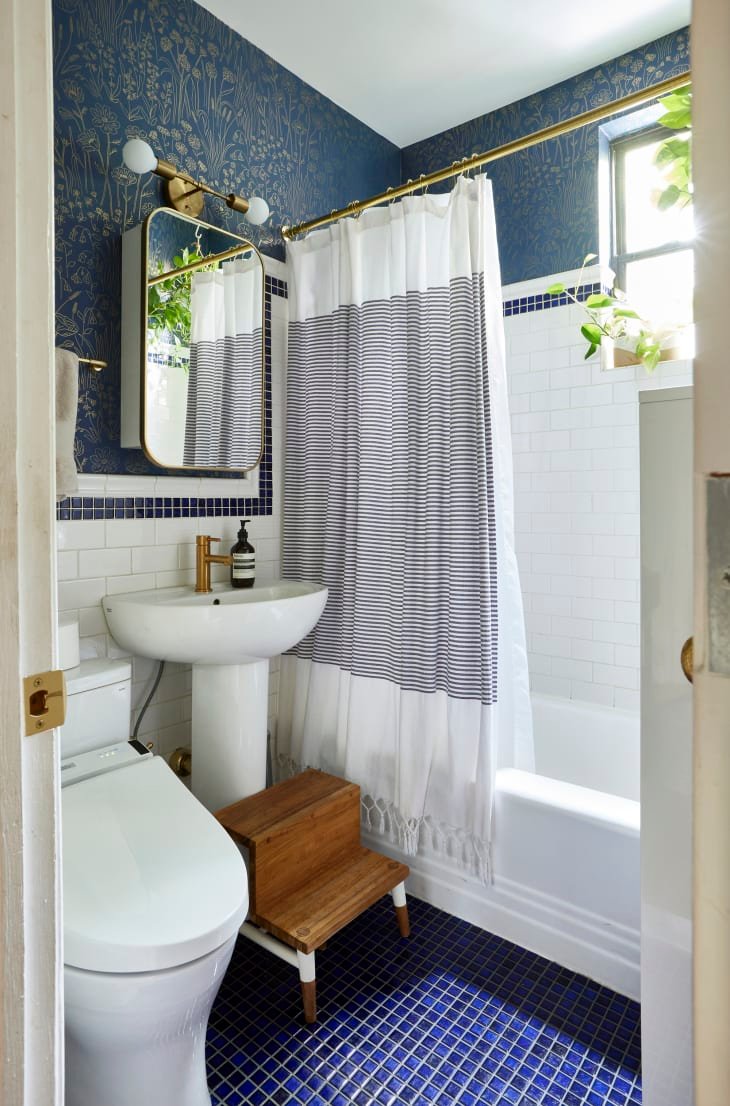 Blue and gold botanical wallpaper in bathroom with blue tiles and brass hardware.