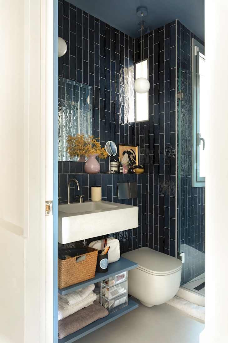 Compact bathroom featuring navy tiled walls, a modern sink, and organized shelves with towels and toiletries.
