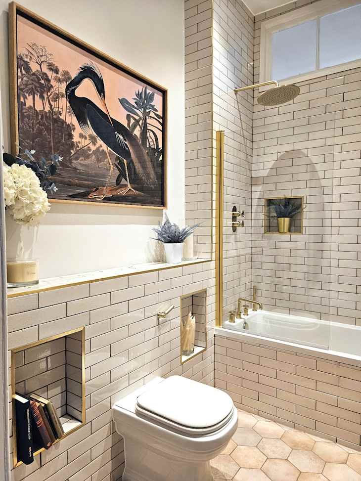 light warm gray tiled bathroom with brass accents and shelves by and over toilet