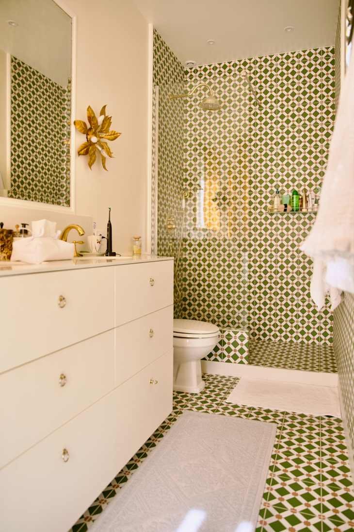 Modern bathroom featuring green and white patterned tiles, a white vanity with gold fixtures, and a glass shower.