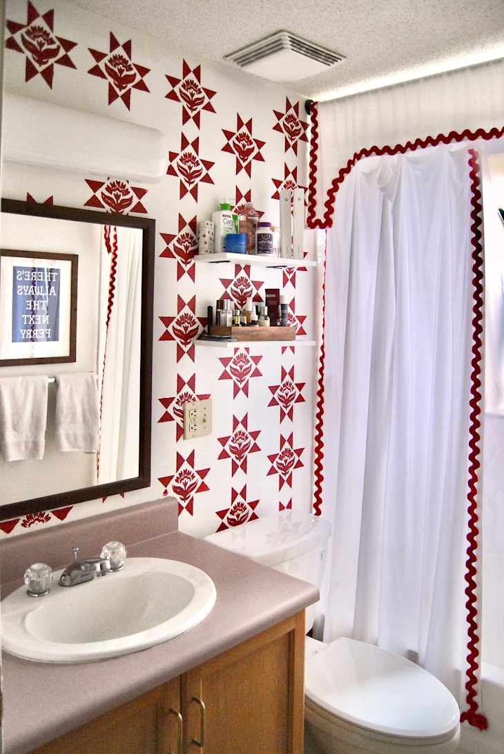 Bathroom with red star-patterned wallpaper, a mirror, sink, and a shower curtain with red trim.