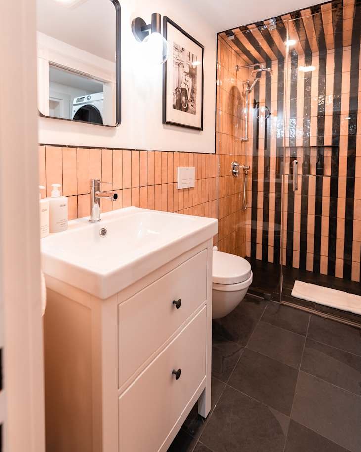 Modern bathroom featuring a white vanity with two drawers, orange tiled walls, a glass shower, and a wall-mounted mirror.